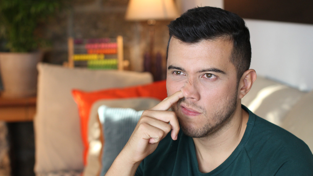 Young man picking his nose while sitting on a couch