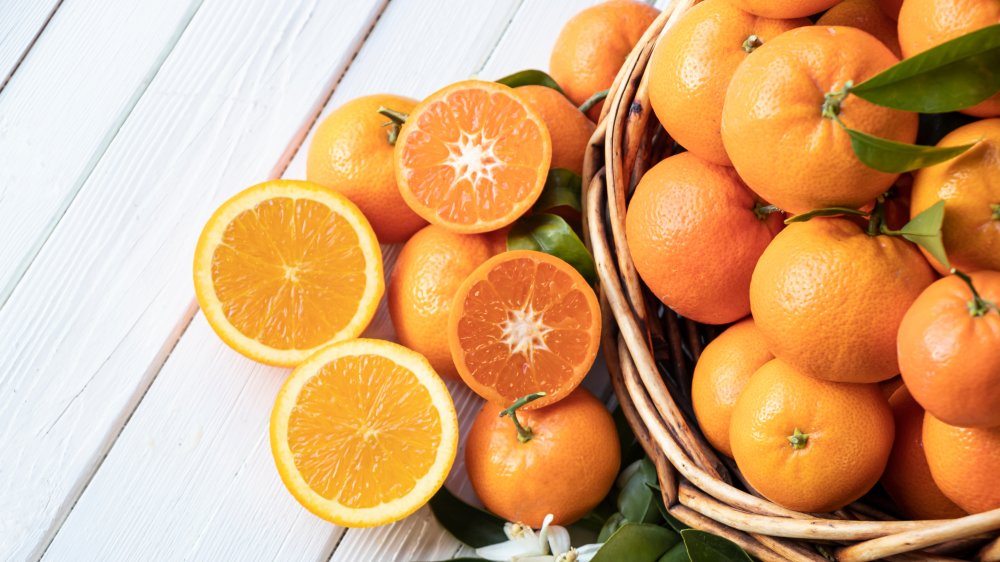 Varieties of oranges with green leaves on white wood table