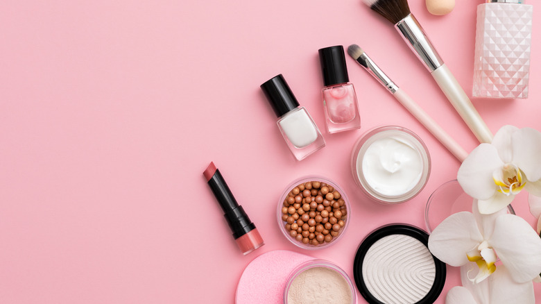 variety of makeup items on a pink background with flower