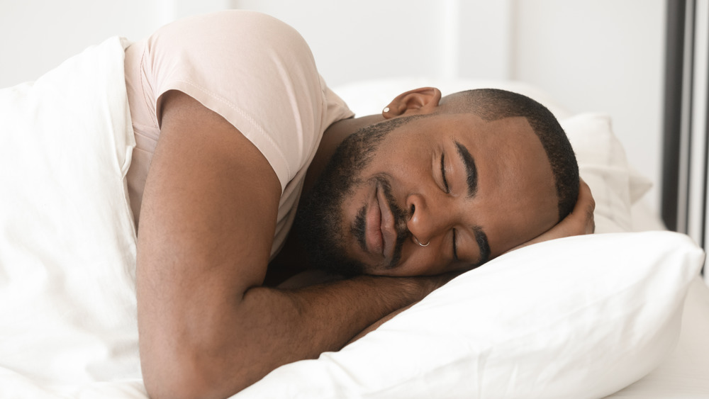 Serene calm handsome young black man sleeping well alone on orthopedic soft pillow under warm duvet, african american guy lying asleep in comfortable cozy bed enjoy good night peaceful healthy sleep