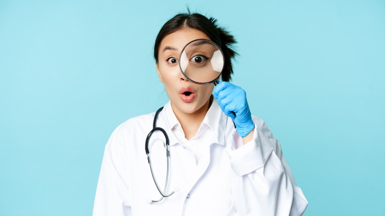  a doctor holds magnifying glass up to her eye