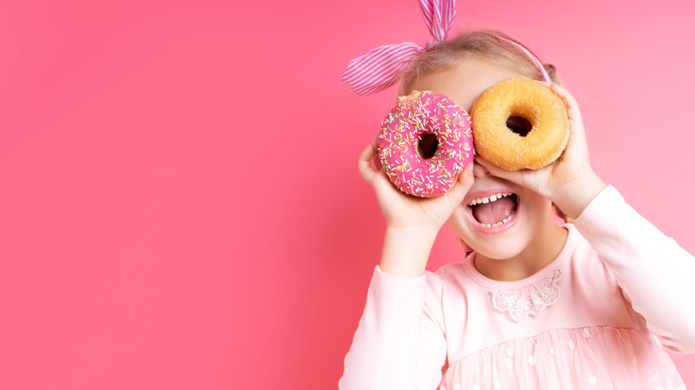 A young girl using donuts as glasses with an all pink background 