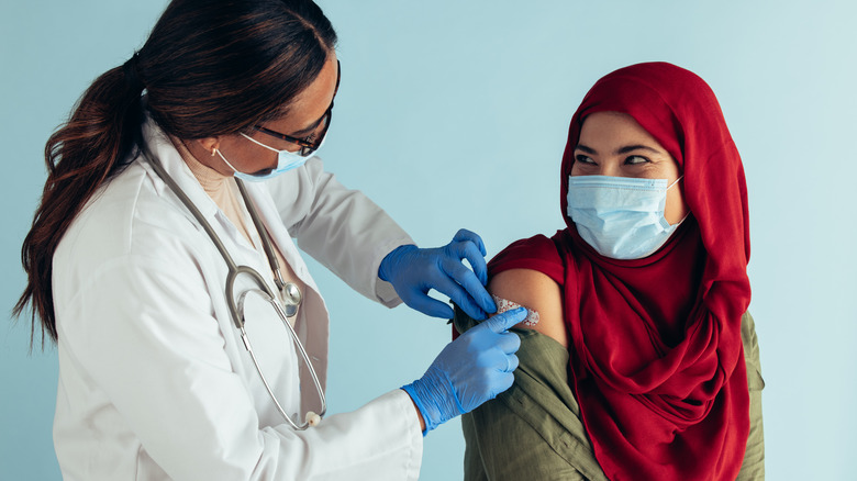 Woman with hajib and face mask getting COVID-19 vaccine from female physician with face mask