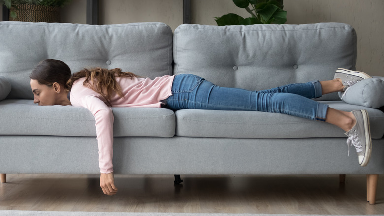 A young woman fully dressed lying face down on her couch 