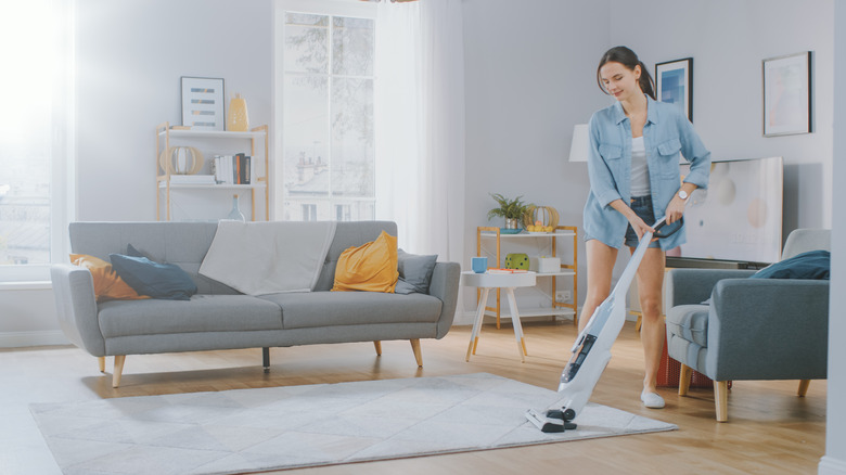 Young woman is vacuuming her carpet