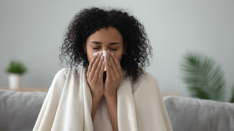 A woman sits on a couch blowing her nose