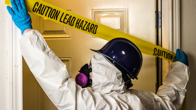 Man in a hazard suit positing a warning across a door painted with lead-based paint 