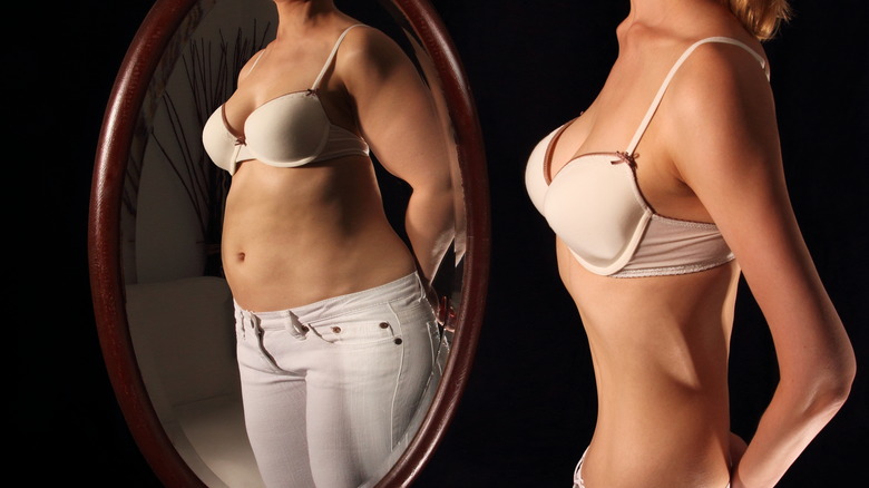 a thin woman looks in the mirror and sees a larger body 