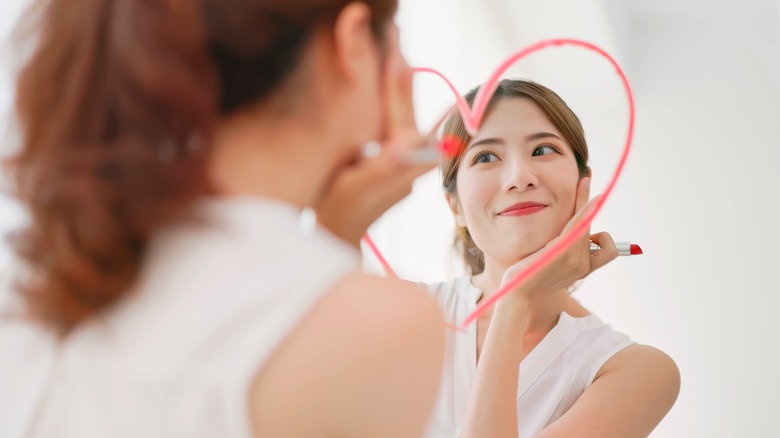 woman draws heart around her face in mirror