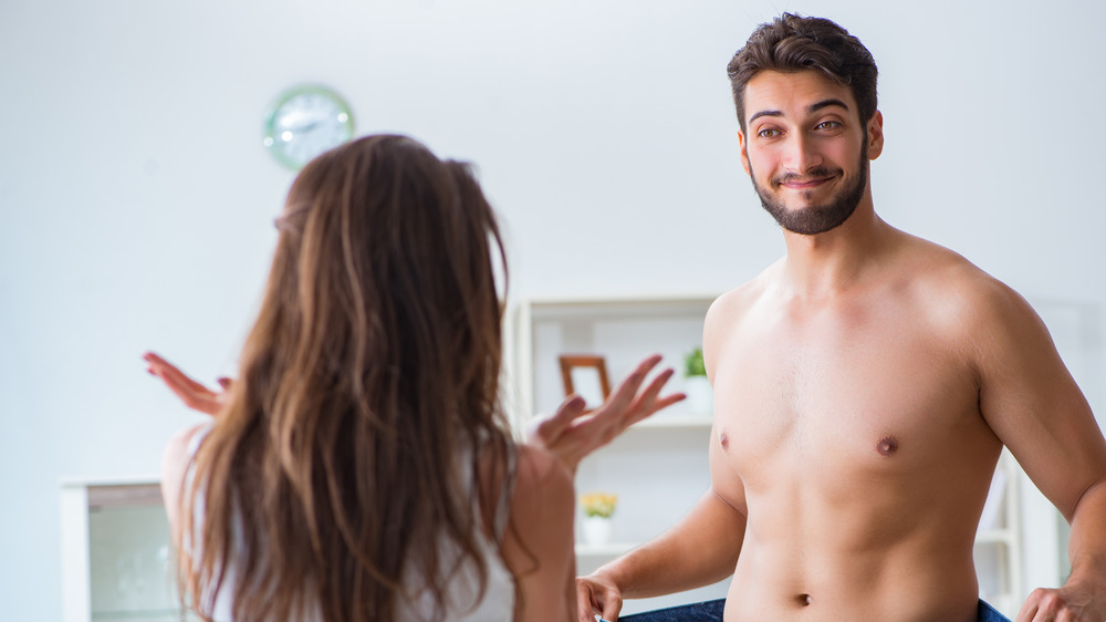 A man showing his partner how much weight he's lost around his waste 