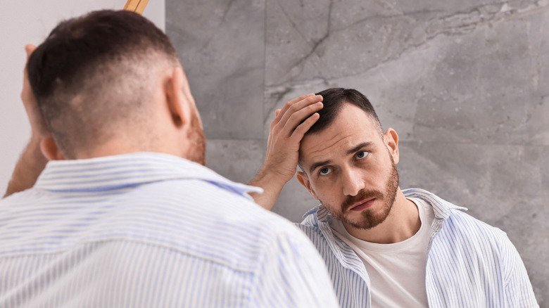 man with thinning hair looking in mirror at home