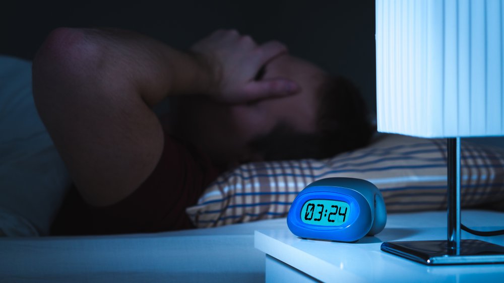 Alarm clock and sick man in bed can't sleep