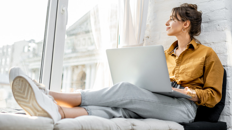 Woman working on laptop by window