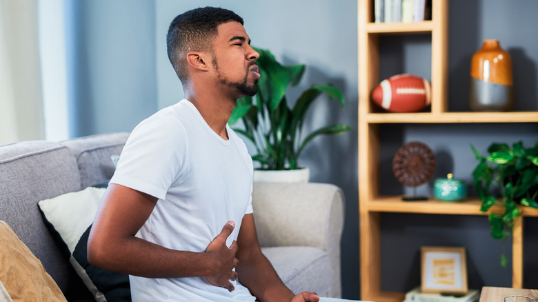 man wincing with nausea while sitting on the couch