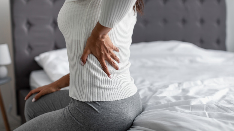 Woman sitting on a bed with her hand on the left side of their lower back