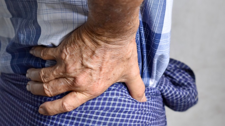 Older man with hand on lower left back