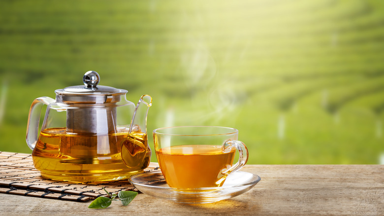 A cup of green tea next to a teapot