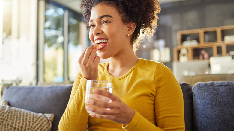 young woman smiling while taking vitamins at home