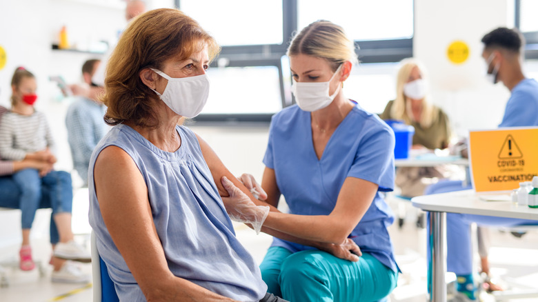 Person with red hair and blue sleeveless shirt getting vaccinated in left arm