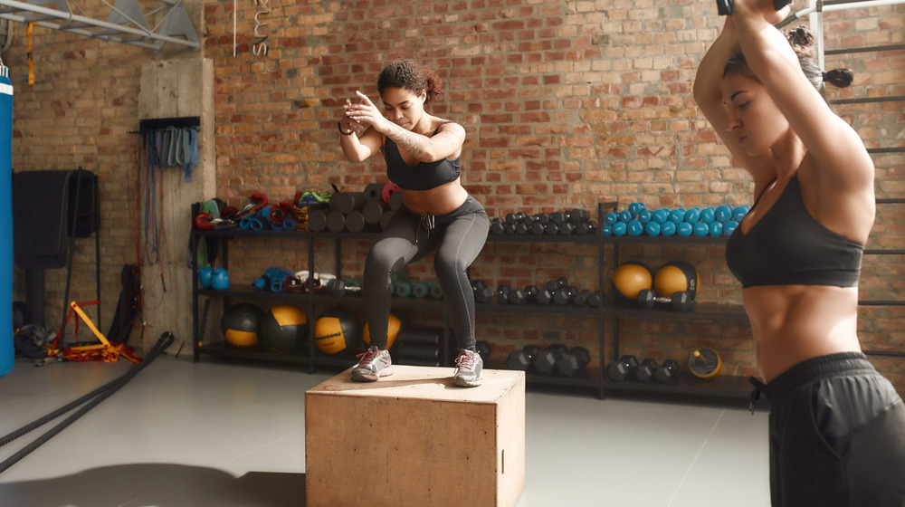 Two women doing box jumps in a gym
