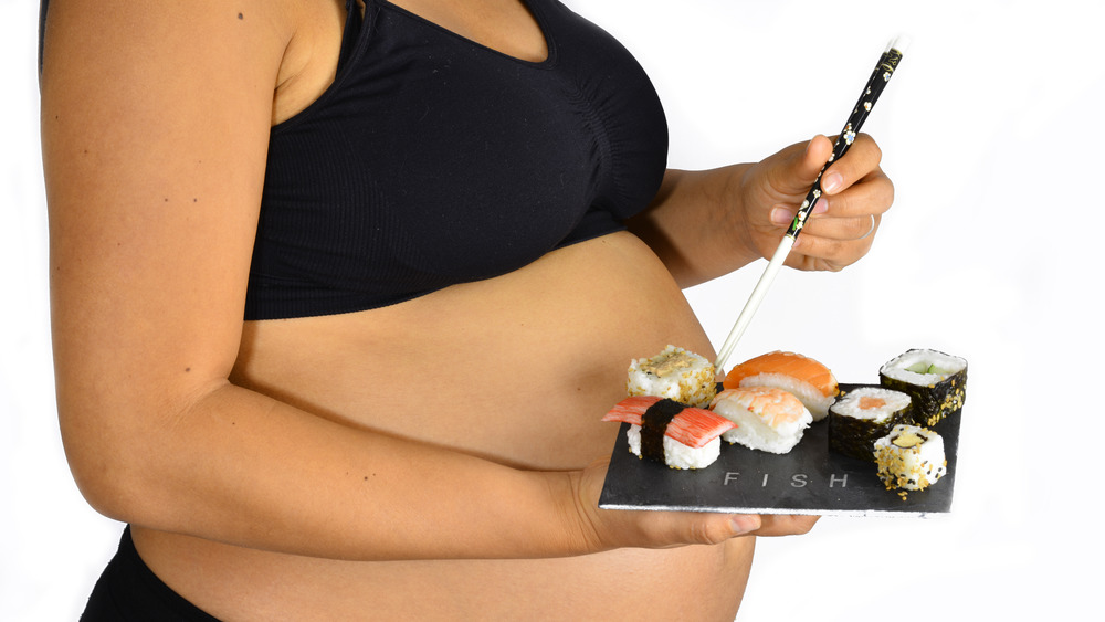 A pregnant woman holding a tray of sushi