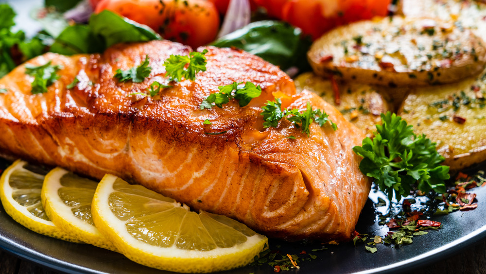 A portion of cooked salmon on a plate with potatoes and a salad