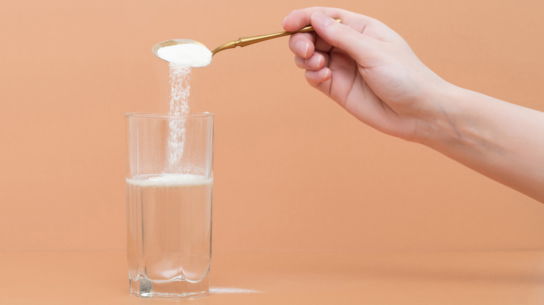 woman pouring collagen powder into a glass