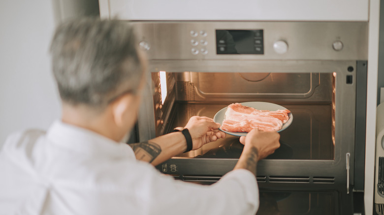 man putting frozen meat into microwave
