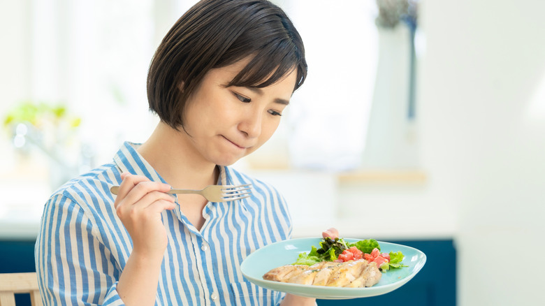 woman looking skeptically at microwaved chicken on her plate