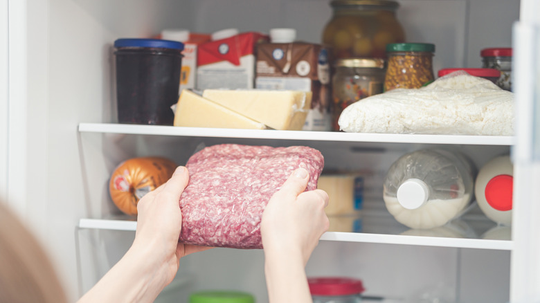 person putting frozen meat into fridge
