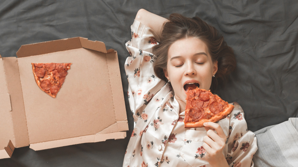 woman eating pizza in bed