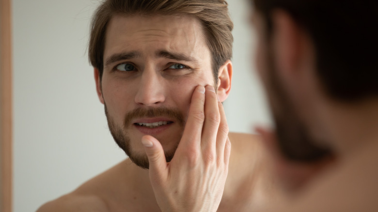 man looking at skin in mirror