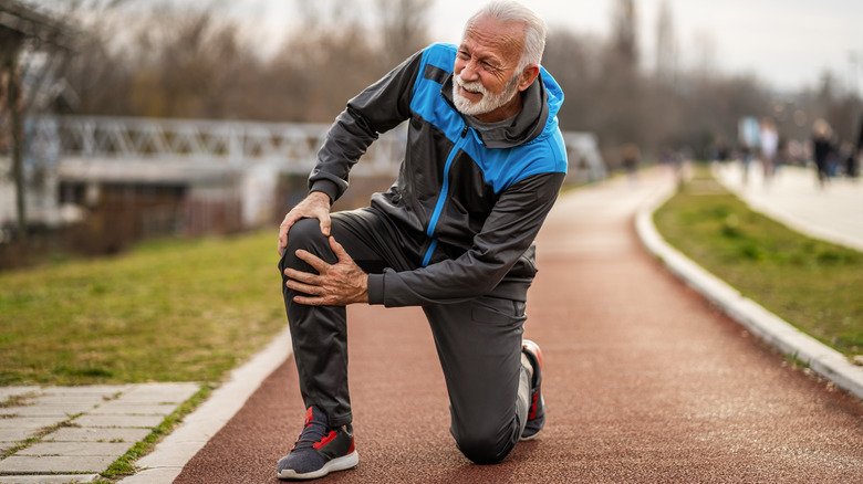 Senior man holding knee on a track