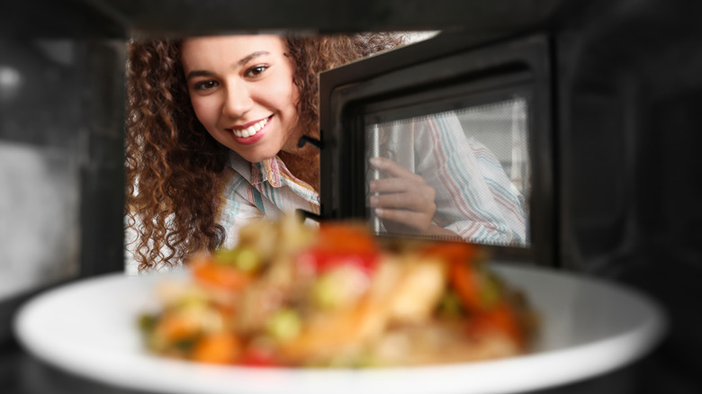 woman looking in microwave oven at food on plate