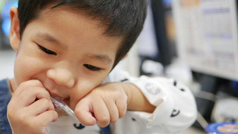 little boy tearing at a straw package with his teeth 