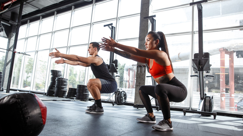 Man and woman performing squats in the gym