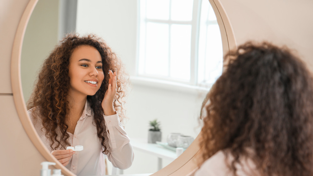 Woman putting in contact lenses while looking in a mirror