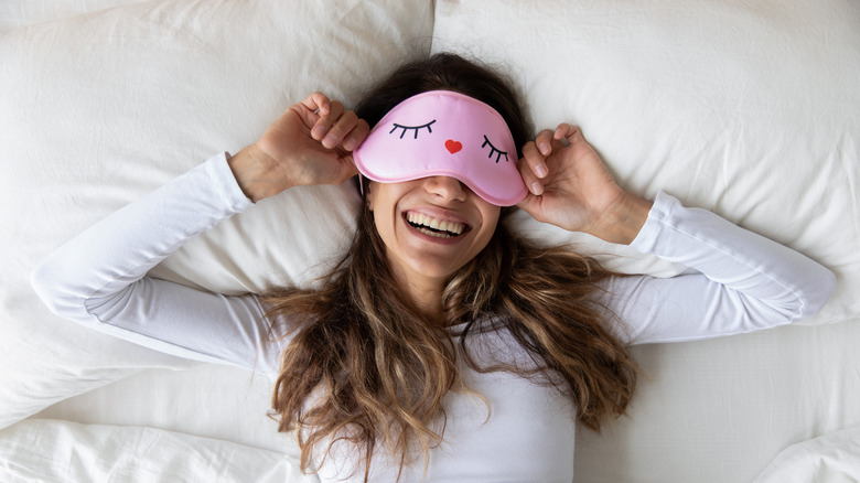 Woman smiling with pink sleep mask over eyes, lying in bed