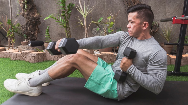 Fit man does sit-ups holding weights on black mat
