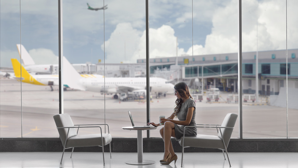 a woman drinking coffee on her laptop at an airport 