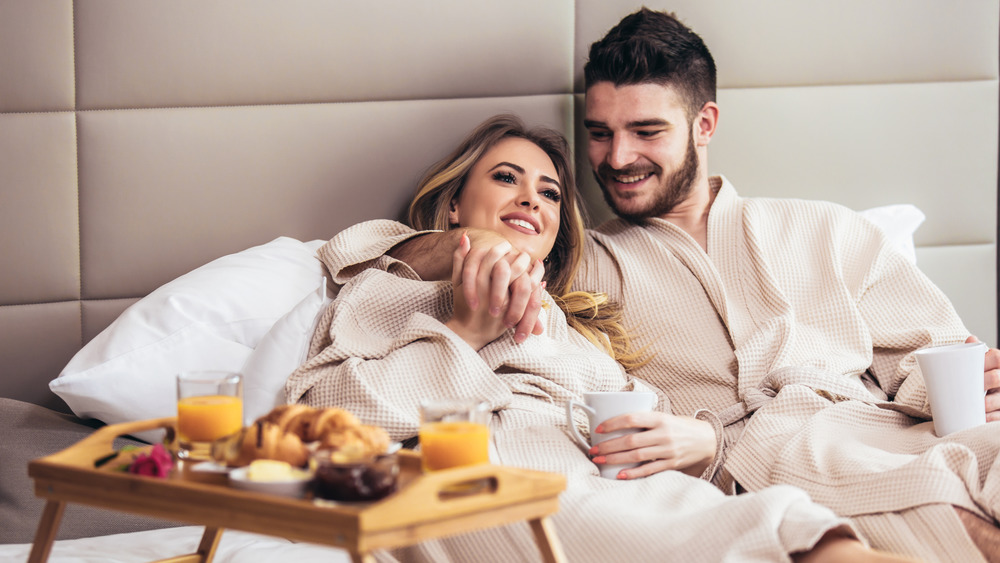 happy couple in robes eating in bed 