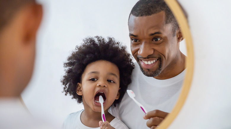 Father and child brushing teeth in the mirror