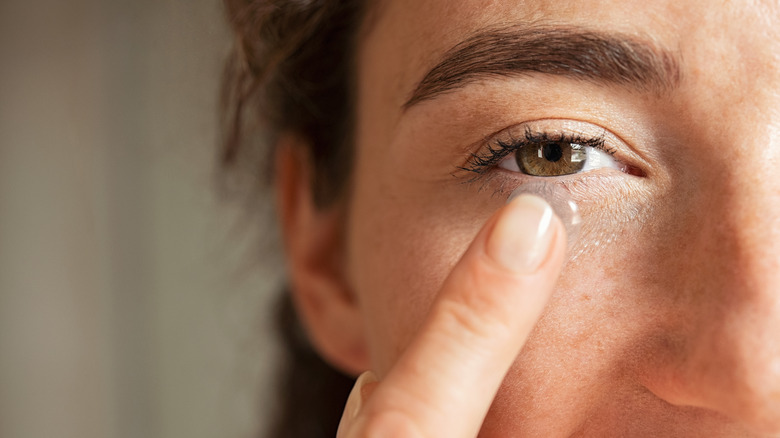 A woman holds a contact lens to her eye