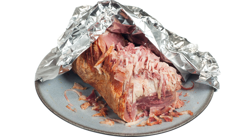 Chunk of ham sitting on plate partially wrapped in tin foil