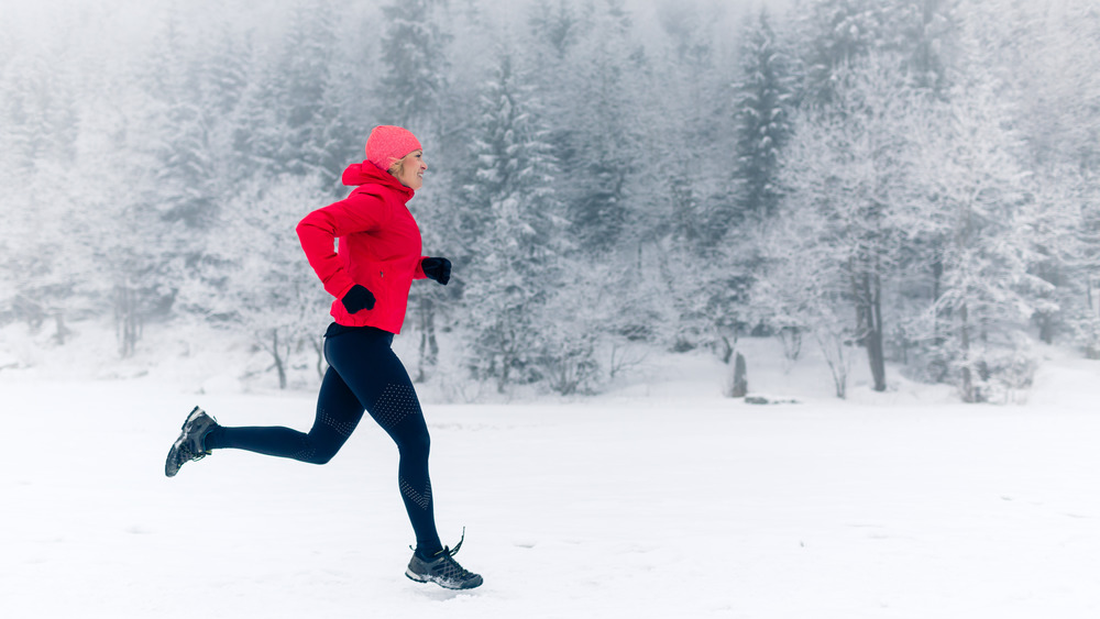 Winter running athlete woman on cold run jogging fast with speed and sprint on outside workout wearing warm clothing gloves, winter tights and wind jacket in snow weather.