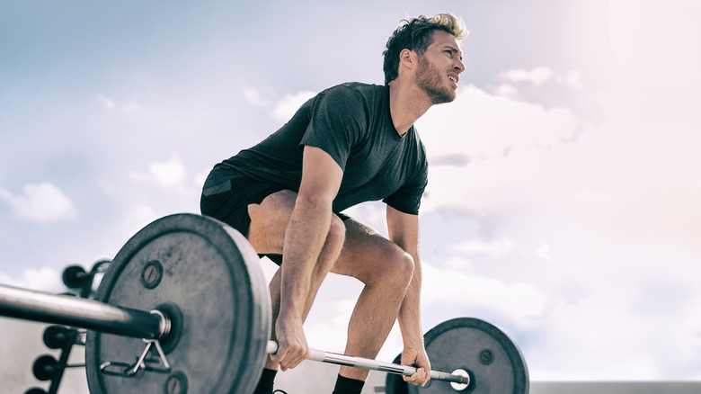 man lifting heavy barbell outdoors