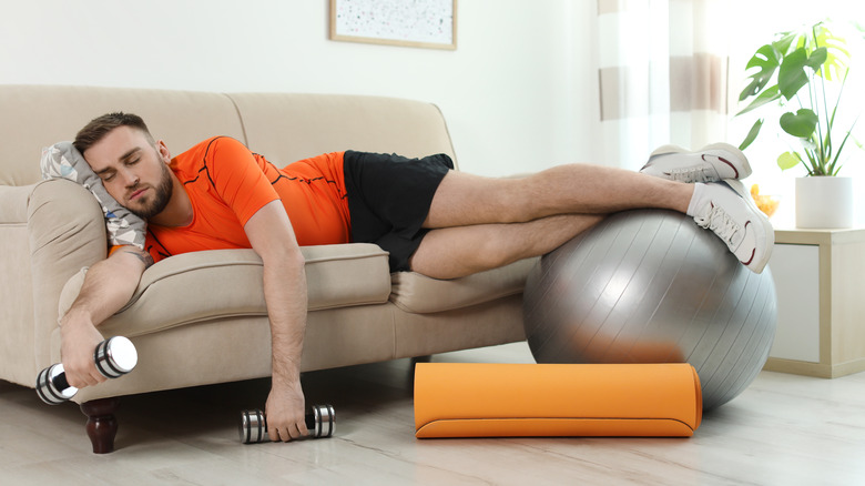 A man lies on a couch holding exercise equipment