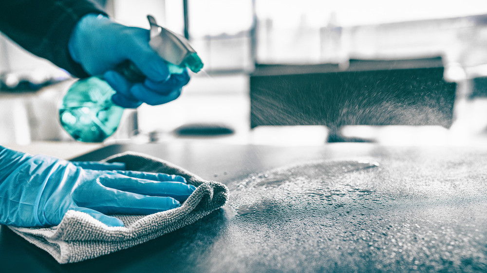 Gloved person cleaning with spray bottle and cloth