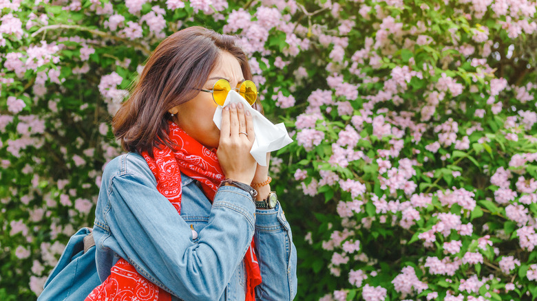 woman blowing her nose while surrounded by flowers