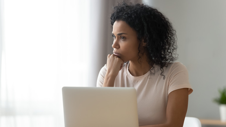 Woman sitting at computer stares off into the distance with her chin on her hand